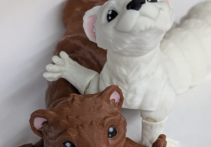 Two 3d printed toy ferrets one is brown and the other is white with pink ears on a soft white background