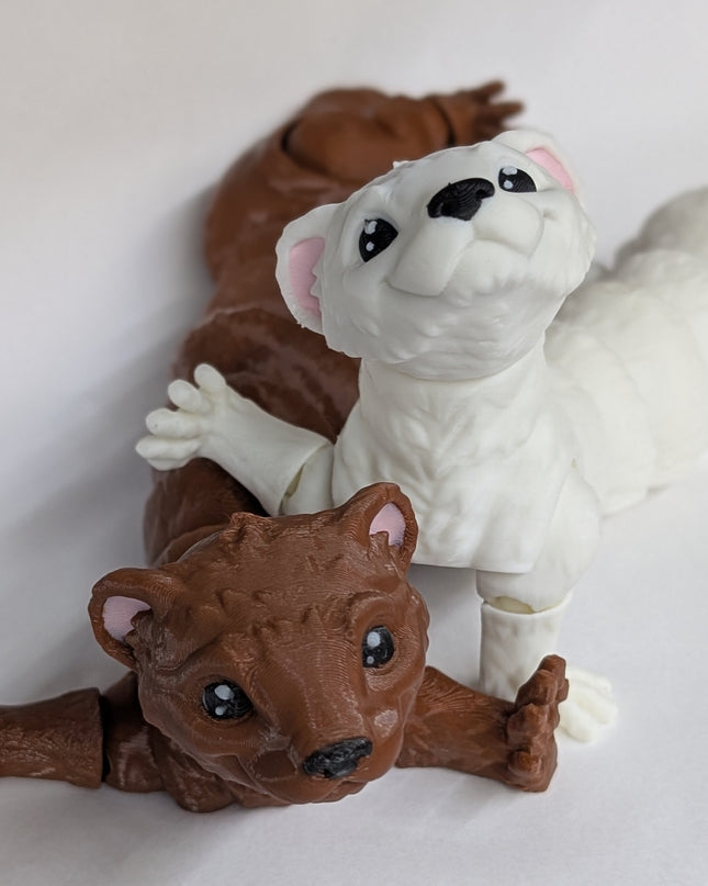 Two 3d printed toy ferrets one is brown and the other is white with pink ears on a soft white background