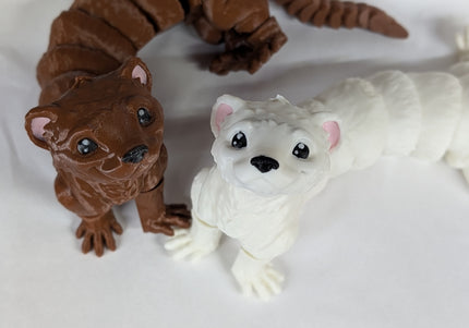 Two 3d printed toy ferrets one is brown and the other is white with pink ears on a soft white background