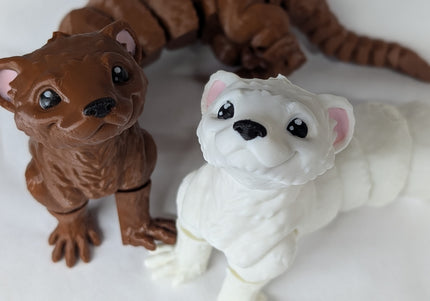 Two 3d printed toy ferrets one is brown and the other is white with pink ears on a soft white background