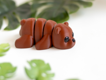 Small brown bear figurine on a white surface with green leaves in the background