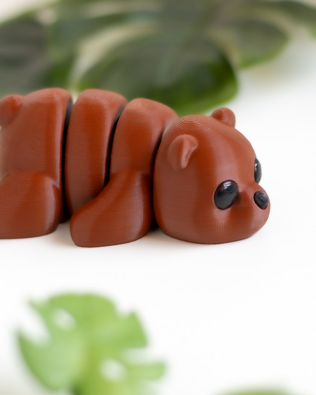 Small brown bear figurine on a white surface with green leaves in the background