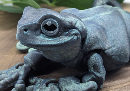 Metallic blue frog sculpture on a wooden surface with green leaves in the background