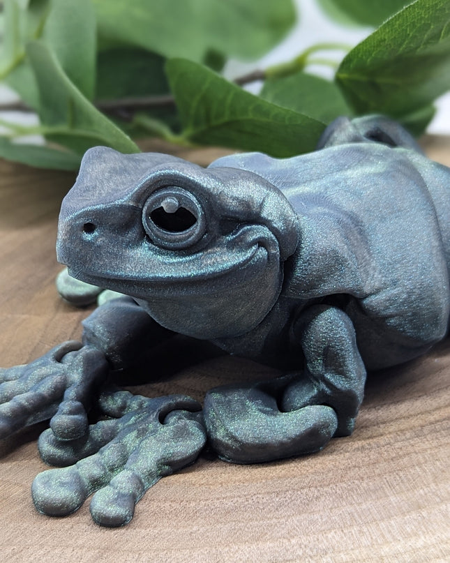 Metallic blue frog sculpture on a wooden surface with green leaves in the background