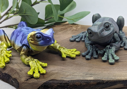 Two colorful frog figurines on a wooden surface with leaves in the background