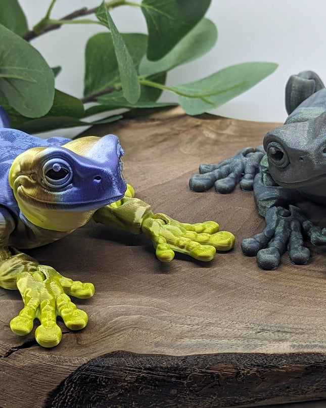 Two colorful frog figurines on a wooden surface with leaves in the background