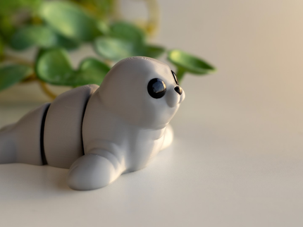 Small gray seal figurine on a light surface with green leaves in the background