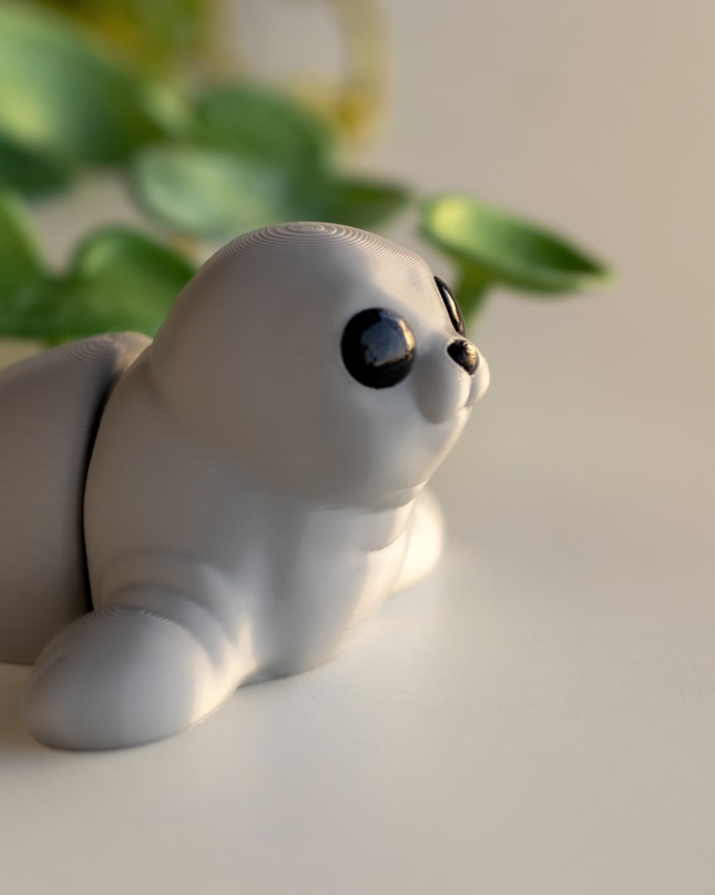 Small gray seal figurine on a light surface with green leaves in the background