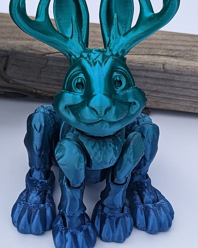 Blue ombre 3d printed jackalope with rabbit-like features on a white background with a wooden log 