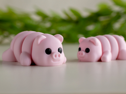 Two pink pig-shaped squishies on a light surface with greenery in the background