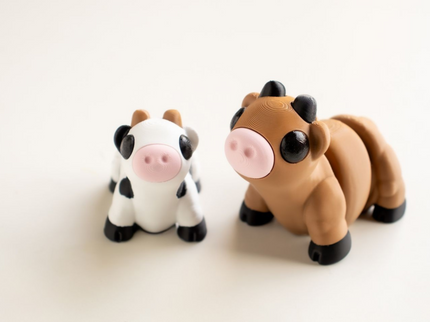 Two toy cow figures, one black and white and one brown and black, on a light beige background.