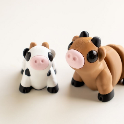 Two toy cow figures, one black and white and one brown and black, on a light beige background.