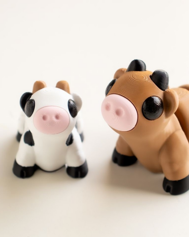 Two toy cow figures, one black and white and one brown and black, on a light beige background.