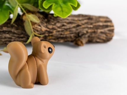 Squirrel-shaped object on a white surface with greenery and wood in the background