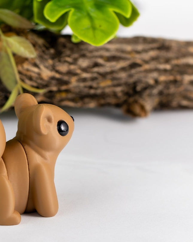 Squirrel-shaped object on a white surface with greenery and wood in the background