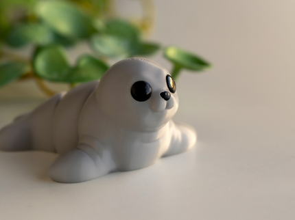 Toy seal figurine on a light surface with green leaves in the background