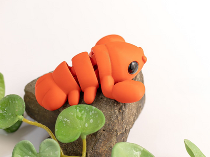 Orange lobster toy on a rock with green leaves on a white background