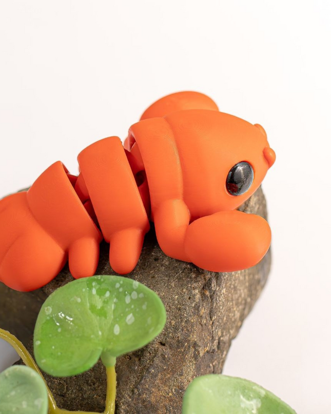 Orange lobster toy on a rock with green leaves on a white background