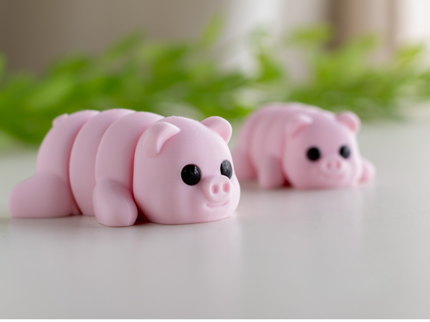 Two pink pig-shaped toys on a light surface with green leaves in the background