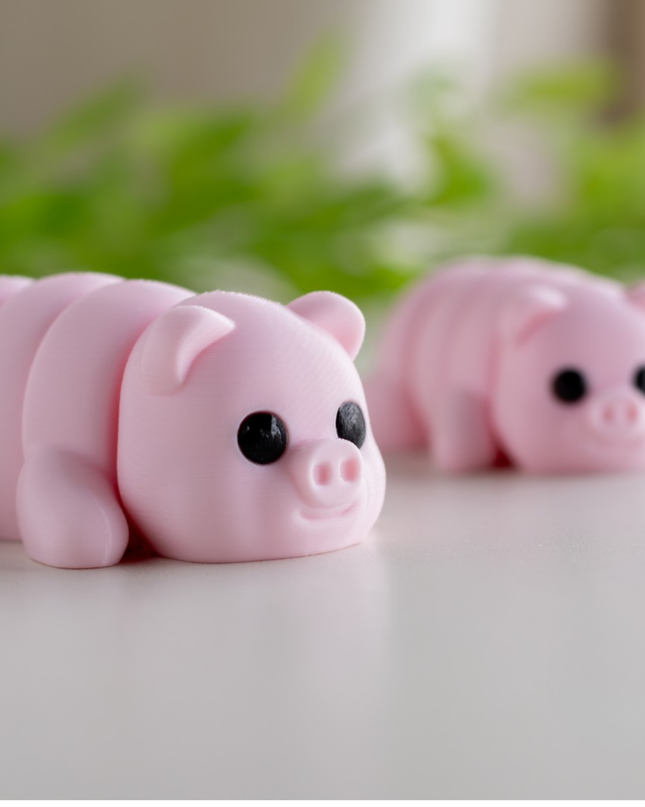Two pink pig-shaped toys on a light surface with green leaves in the background