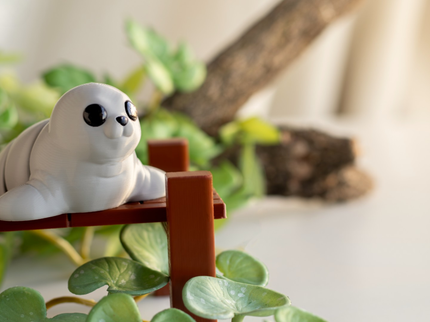 White seal figurine on a small wooden platform with green plants in the background