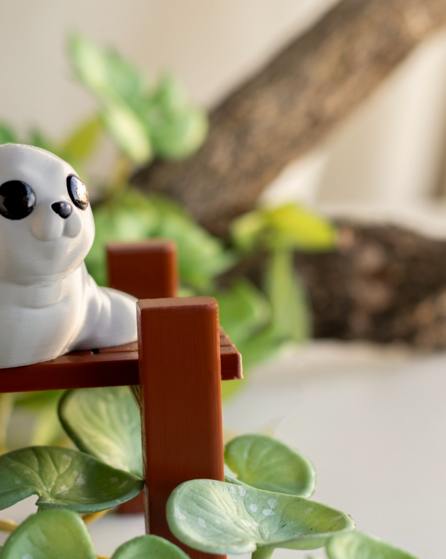 White seal figurine on a small wooden platform with green plants in the background