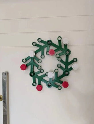 Green wreath-shaped wall hook with red accents on a white wall.