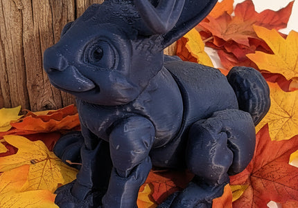 Blue shiny jackalope figurine on a white surface with a wooden stick in the background with colourful maple leaves all around