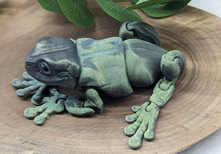 Green frog sculpture on a wooden surface with leaves in the background