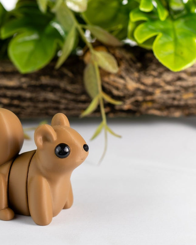 Small brown squirrel figurine on a white surface with green leaves and wood in the background
