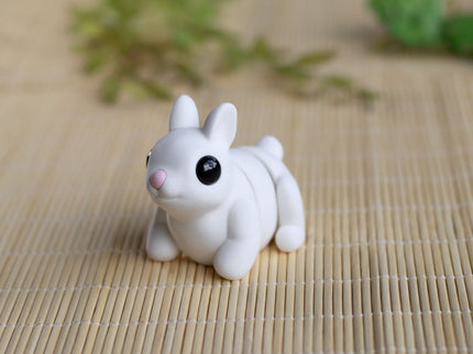 Small white dog figurine on a bamboo mat with greenery in the background