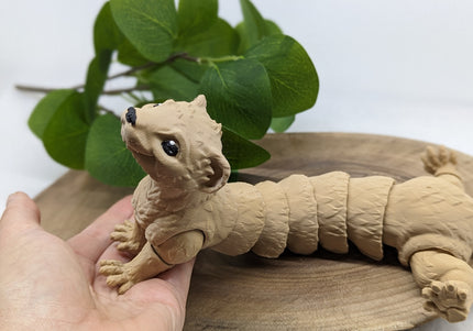 a 3d printed ferret toy leaning on a hand both resting on a wooden stand with a green plant on a soft white background