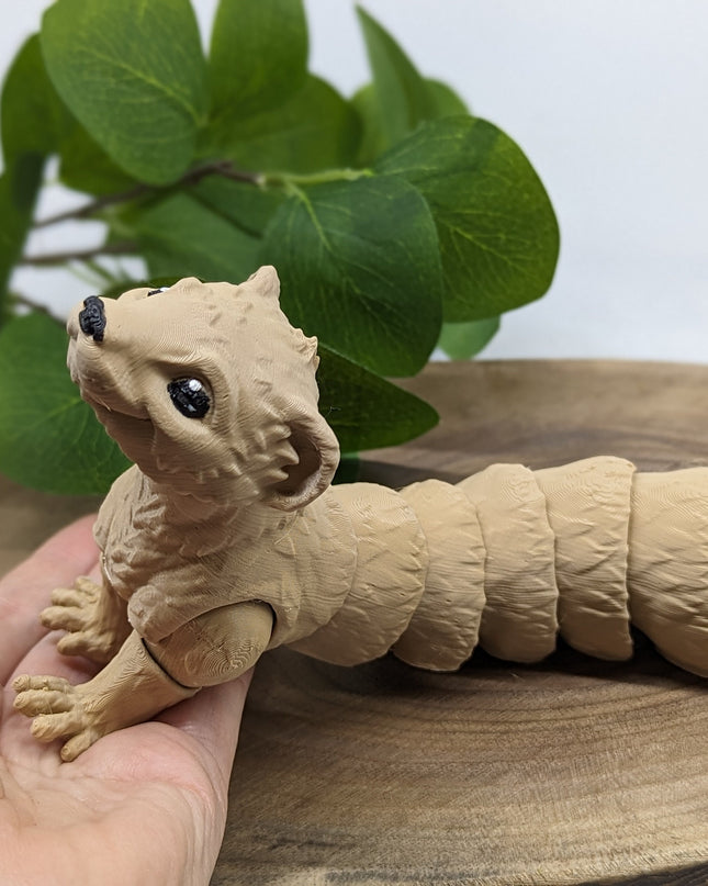 a 3d printed ferret toy leaning on a hand both resting on a wooden stand with a green plant on a soft white background