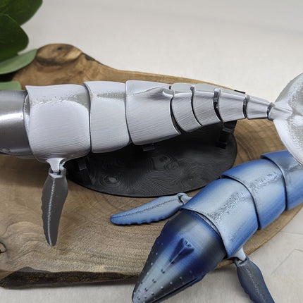 Model of a blue and gray humpback whale  on a wooden surface with a plant in the background.