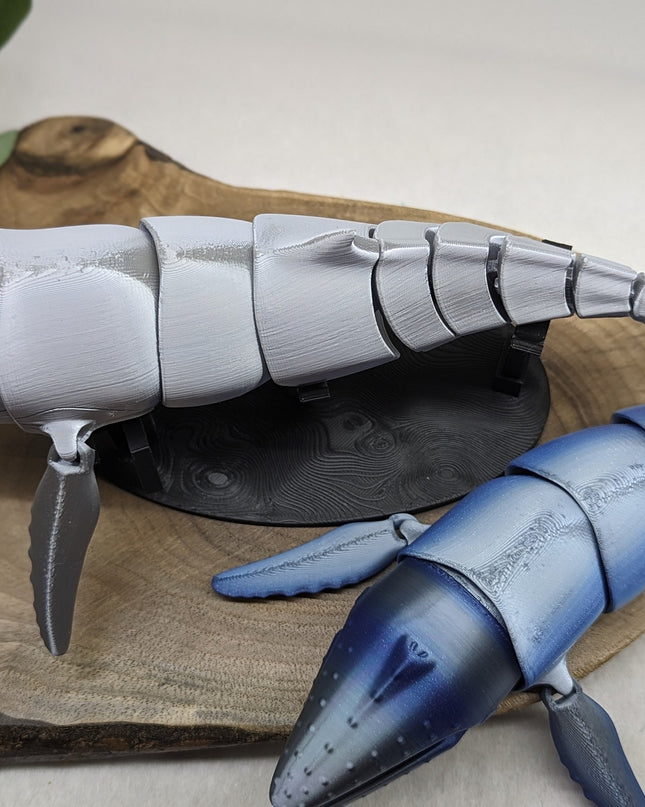 Model of a blue and gray humpback whale  on a wooden surface with a plant in the background.