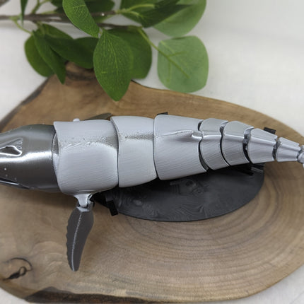 Metallic humpback whale sculpture on a wooden surface with green leaves in the background
