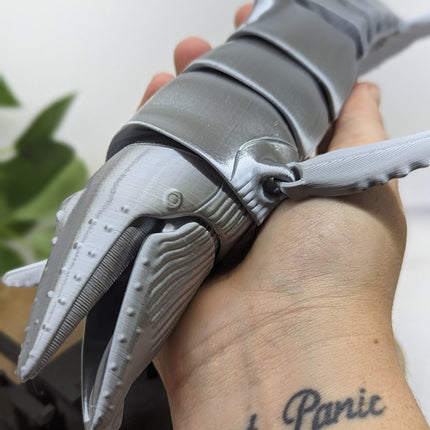 Metallic grey whale held by a person with 'Don't Panic' tattoo