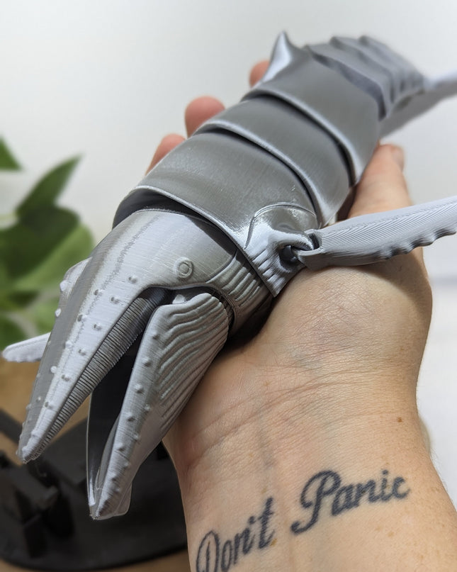 Metallic grey whale held by a person with 'Don't Panic' tattoo