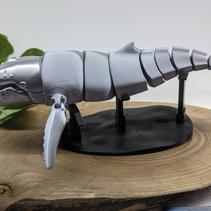 3D-printed whale model on a wooden surface with a plant in the background
