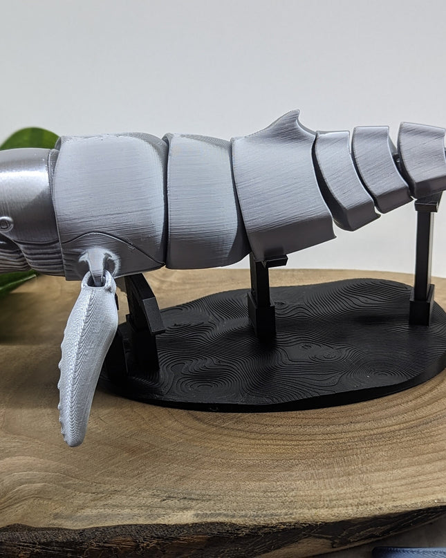 3D-printed whale model on a wooden surface with a plant in the background