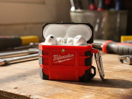 Red and black Milwaukee Air Pod Case open with ear buds, on a workbench with tools in the background