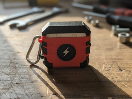 Red and black Milwaukee Air Pod Case closed, on a workbench with tools in the background