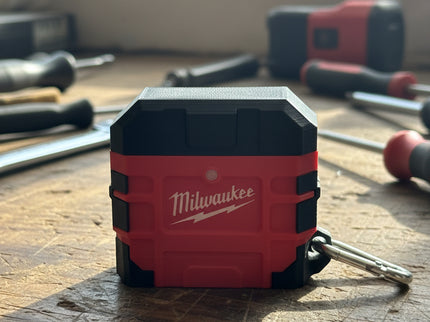 Red and black Milwaukee Air Pod Case closed, on a workbench with tools in the background