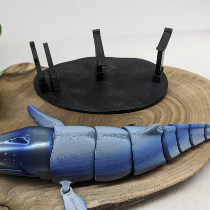 Blue whale-shaped object on a wooden bae with a black stand in front of a white background
