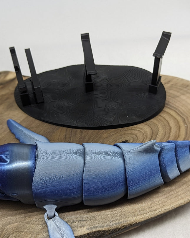 Blue whale-shaped object on a wooden bae with a black stand in front of a white background