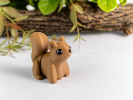 Small brown squirrel figurine on a white surface with greenery in the background