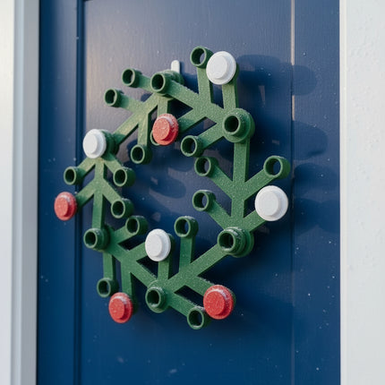 Green wreath-shaped object with red and white accents hanging on a bright blue door