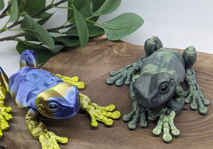 Two colorful frog figurines on a wooden surface with green leaves in the background.