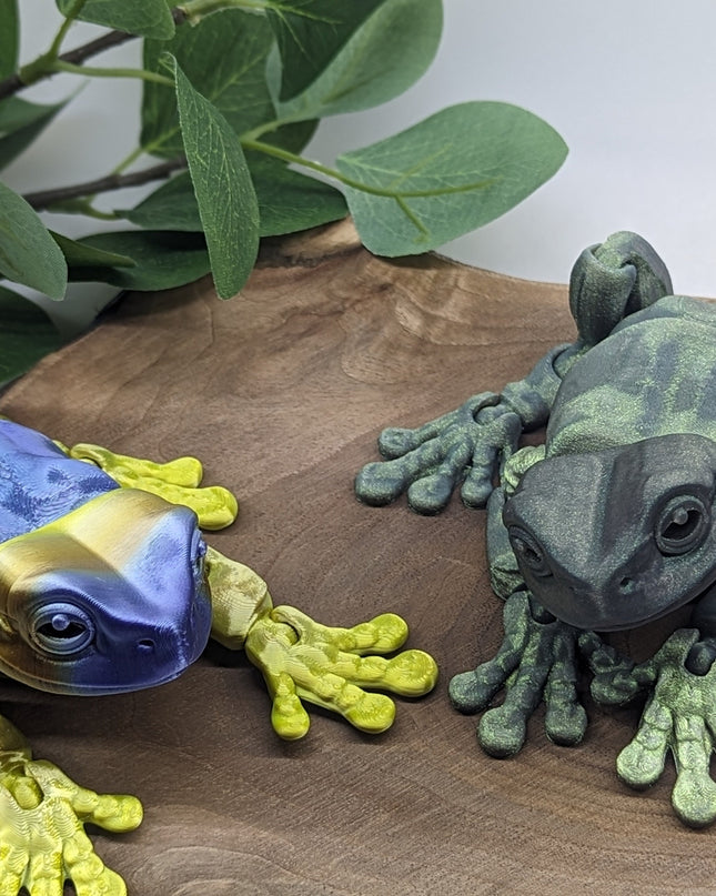 Two colorful frog figurines on a wooden surface with green leaves in the background.