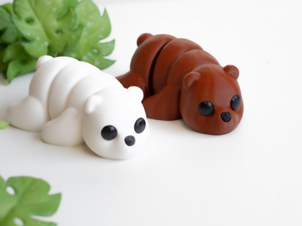 Two small animal figurines, one white and one brown, on a white surface with green leaves in the background.